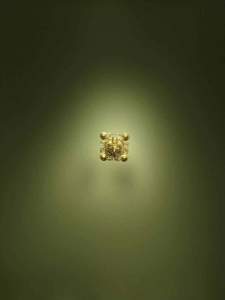 Small gold artifact from the Gold Museum in Bogota displayed against a green background