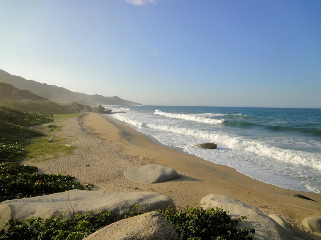 Sunny beach in Tayrona Park, Santa Marta with mountains and ocean waves.