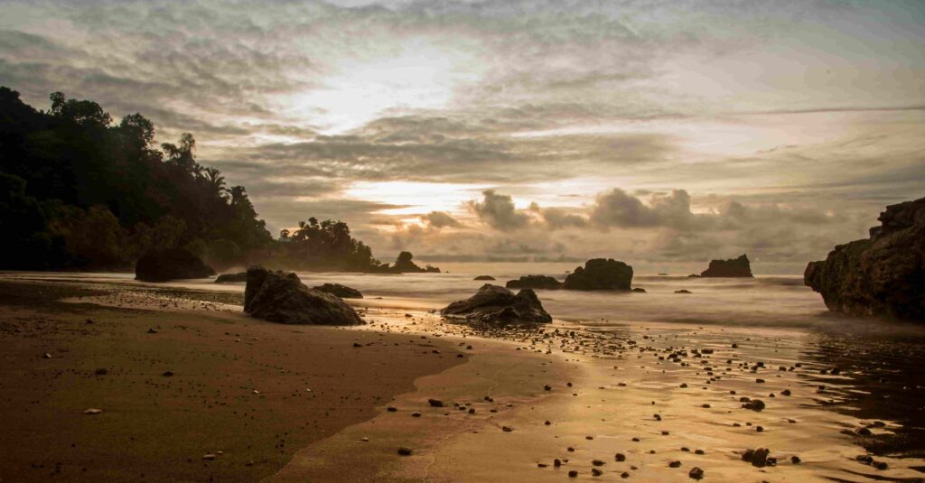 nuqui-colombia-beach-sunset-rocks Sunset at a long beach in Nuqui, pacific coast in Colombia, with large rocks, sea, and lush jungle background.